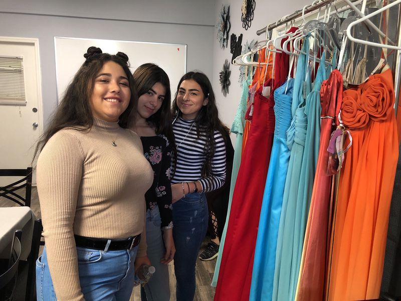 Emely González, Dennisse Marie González y Yamarie González posan frente a los trajes que fueron donados para las quinceañeras. (Jennifer A. Marcial Ocasio / El Sentinel)